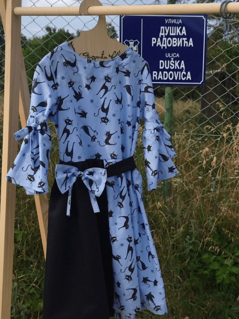 Haljina sa motivom mačaka (ručni rad) okačena na ogradu na kojoj piše naziv ulice - ulica Duša Radovića